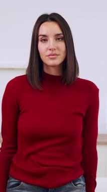 İş yerindeki masanın önünde kollarını kavuştururken kameraya gülümseyen kendine güvenen genç bir kadının dikey HD videosu. Girişimciler ve iş konsepti.