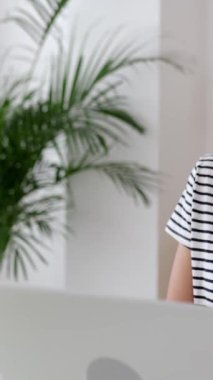 Evdeki oturma odasında çalışırken dizüstü bilgisayar kullanan gündelik giysili güzel bir kadının dikey HD videosu. Serbest çalışanlar ve merkez ofis konsepti.