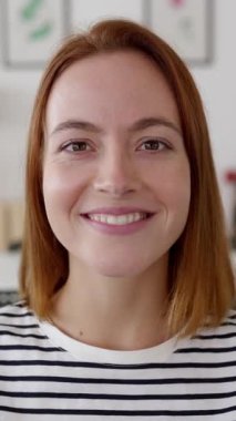 Genç ve güzel bir kadının dizüstü bilgisayardaki görüntülerini dinlerken çekilmiş dikey HD videosu. Vesikalık kamera görüntüsü. Sanal toplantı konferansına katılan gülümseyen kadın portresi..
