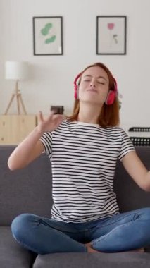 Evdeki kanepede dans eden mutlu genç kadının dikey HD videosu. Ev hayatı ve mutluluk kavramı