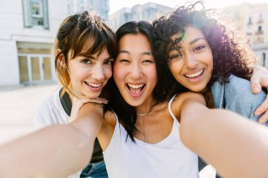 Üç çok ırklı genç kadın şehir sokaklarında eğleniyor. Milenyum arkadaş grubu yaz tatilinin tadını çıkarıyor açık havada selfie çekiyorlar. Arkadaşlık ve gençlik kavramı.