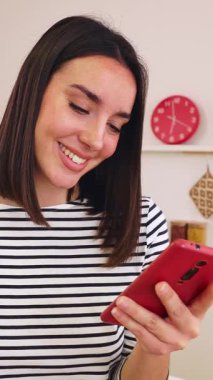 Modern bir mutfakta cep telefonunu kullanırken portakal suyu içen, sağlıklı bir yaşam tarzını somutlaştıran ve bağlı kalan genç kadının dikey HD videosu. Sosyal medya kavramı