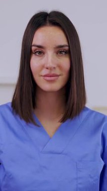 Kendine güvenen genç bir hemşirenin dikey video portresi çapraz kollarla gülümseyen, parlak bir tıbbi ofis ortamında profesyonellik ve sağlık uzmanlığı sergileyen. Sağlık çalışanları kavramı