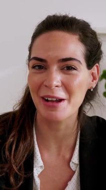 Dikey HD video. Güzel bir iş kadınının iş yerinde dizüstü bilgisayarla konuştuğu görüntüler. Zeki girişimci kadın kameraya bakıyor ve sanal görüşme üzerine sohbet ediyor..