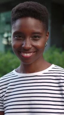 Genç ve güzel Afrikalı bir kadının dikey HD portresi. Kamera karşısında gülümseyen bir kadın.