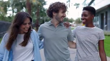 Dışarıda yürürken birbirine sarılan üç farklı arkadaştan oluşan genç bir grubun ön görüntüsü. Milenyum kuşağı insanları yaz tatilinde eğleniyor..