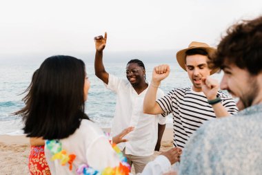 Neşeli bir grup genç arkadaş yaz plaj partisinde eğleniyor, birlikte okyanus kenarında dans edip gülüyorlar, arkadaşlığı ve çeşitliliği kutluyorlar.