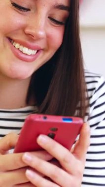 Genç mutlu bir kadının evdeki mutfakta cep telefonu kullanıp uygulamadan sosyal medya içeriğini izlerken eğlendiği dikey HD videolar. Teknoloji ve ev hayatı kavramı