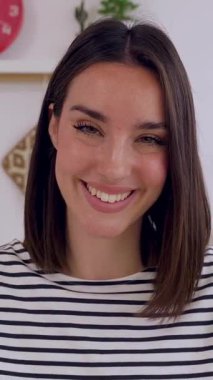 Dikey HD video. Mutfakta kameraya gülümseyen güzel bir kadının portresi. Millennial çekici kadın dişlek gülümseme sergiliyor, evde pozitif ve kendinden emin hissediyor.. 
