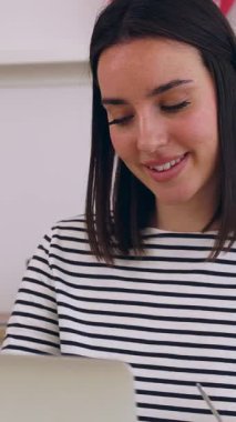 Genç mutlu kadının sabahları kahve içerken evde dizüstü bilgisayarla çalışırken çekilmiş dikey HD videosu. İnternette öğrenen kız öğrenci. Eğitim ya da iş konsepti