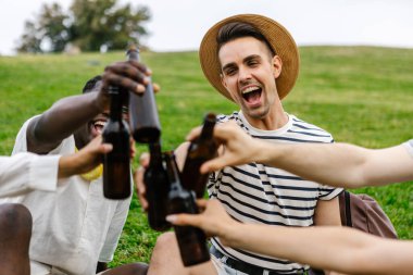 Çeşitli arkadaşlar şehir parkında yaz pikniğinin tadını çıkarırken bira şişeleriyle tezahürat yapıyorlar.