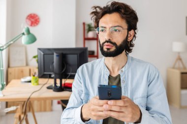 Stüdyo ofisinde cep telefonu tutan düşünceli genç, profesyonel yaratıcı adam. Teknoloji ve iş konsepti.