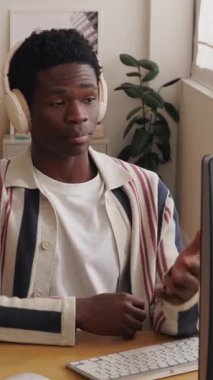 Genç, mutlu, kulaklık takan, bilgisayar kullanan ve video konferansı yapan Afrikalı bir çocuğun dikey HD videosu. Eğitim, iş ve e-öğrenim kavramı