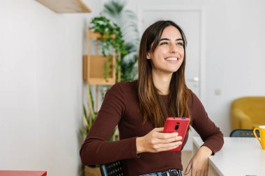 Evde akıllı telefon kullanan mutlu genç bir kadın. Teknoloji konsepti.