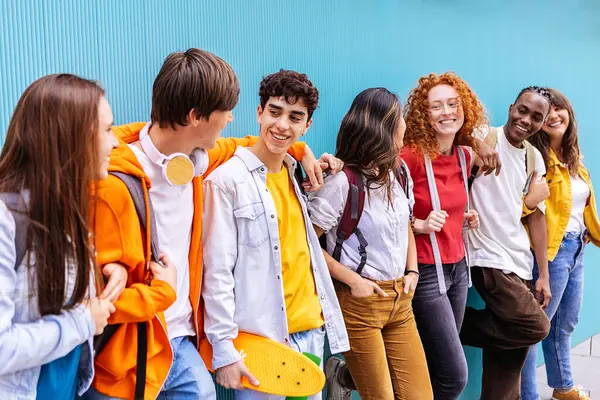 Kampüs duvarına yaslanmış mutlu genç öğrenciler birlikte takılıyor. Gençlik ve eğitim kavramı