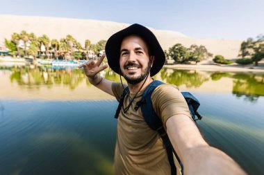 Mutlu genç gezgin, Peru 'da tatilin tadını çıkarırken Huacachina vahasında selfie çekiyor.