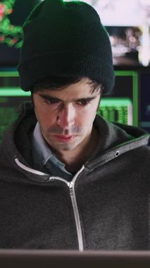 Ana ofisinden kurumsal sunuculara girmeye odaklanan genç hacker 'ın dikey HD videosu, yeşil kod gösteren birden fazla bilgisayar ekranı ile çevrili.