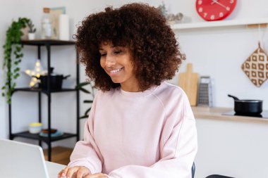 Genç, mutlu, Afro-Amerikan bir kadın mutfak masasında dizüstü bilgisayar kullanıyor. Ev ve iş konseptinden çalışmak