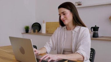 Mutfak masasında dizüstü bilgisayarını kullanarak uzaktan çalışan mutlu genç girişimci kadın. İş konsepti 