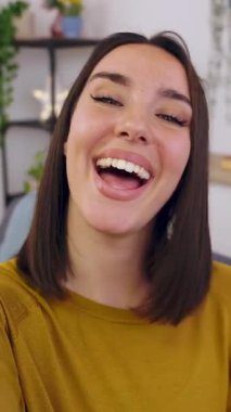 Evdeki kanepede otururken cep telefonuyla video görüşmesi yapan mutlu genç bir kadının dikey HD videosu. Çevrimiçi iletişim kavramı.