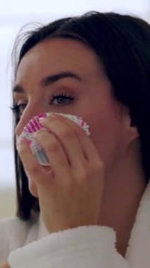 Bornoz giyen mutlu bir kadının makyajı silmek için tekrar kullanılabilir pamuk pedi kullandığını gösteren dikey HD video.