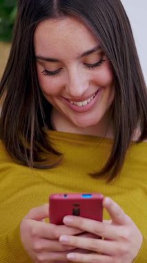 Kanepede oturan mutlu genç kadının dikey HD videosu. Milenyum kadını evde dinleniyor cep telefonundan sosyal medya içeriğini kontrol ediyor. Teknoloji ve eğlence kavramı