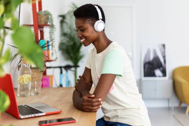 Genç Afrikalı öğrenci internetten öğrenim görüyor. Laptop bilgisayarında video dinliyor. Modern ofis masasında oturuyor.