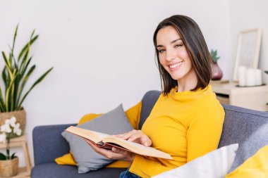 Modern dairedeki rahat koltukta oturmuş kitap okuyan güzel bir kadının gülümseyen portresi..