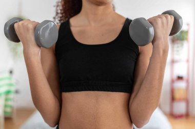 Genç bir kadın evinde ağırlık kaldırıyor, spor ve güç antrenmanlarına odaklanıyor.