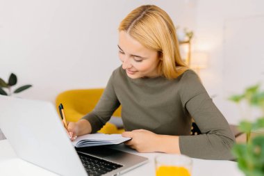 Evde dizüstü bilgisayar kullanırken not alan genç bir bayan öğrenci. Milenyum Avrupalı kadın çevrimiçi sanal video dinlemeyi öğreniyor. İş ve eğitim kavramı.