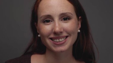 Kameraya gülümseyen, pozitiflik ve kendine güven saçan, kızıl saçlı ve çilli neşeli genç bir kadının yakın çekim portresi. Mutluluk kavramı