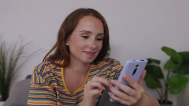 Genç yetişkin bir kadın akıllı telefondan sohbet ediyor ya da cep telefonu uygulamasında evde dinlenen sosyal medya içeriğini izliyor. Cep telefonu kullanan güzel bir kız. Teknoloji ve iletişim konsepti