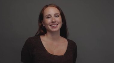 Kızıl saçlı, çilli, kahverengi tişörtlü, gri bir fona hafifçe gülümseyen neşeli genç bir kadının stüdyo portresi. Utangaçlık kavramı