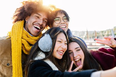 Mutlu genç bir grup insan kışın şehir caddesinde telefonlarıyla selfie çekerken eğleniyor.