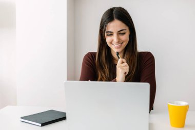 Happy young woman using laptop studying online from home. E-learning and education lifestyle concept.