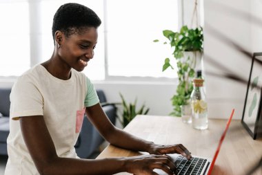 Happy young black woman working on laptop computer sitting on table at home. Education or business concept