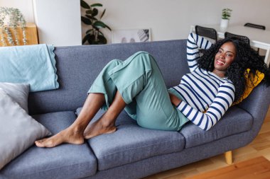 Serene genç siyah kadın rahat bir kanepeye uzanıp evde tatilin tadını çıkarıyor..