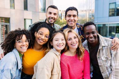 Portrait of young group of diverse people smiling at camera standing outdoor. Happy millennial college students enjoying time together, social gathering and hanging out at city street.