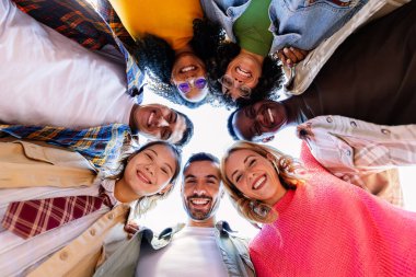 Çember halinde kameraya bakan genç insanların düşük açılı görüntüsü. Dışarıda milenyum dostlarının gülümseyen portresi..