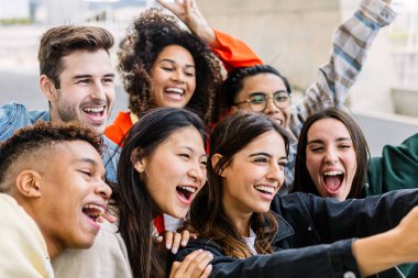 Multiracial group of young students smiling and taking a selfie outdoors, enjoying their time together in an urban setting