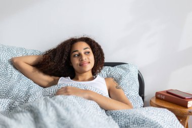 Serene young Latin American woman enjoying a peaceful rest in bed, embracing the comfort of her duvet and pillows, after wake up