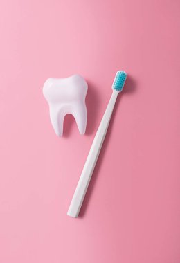 A plastic toothbrush next to a big tooth on a pink background. Oral hygiene. Flat lay, top view.