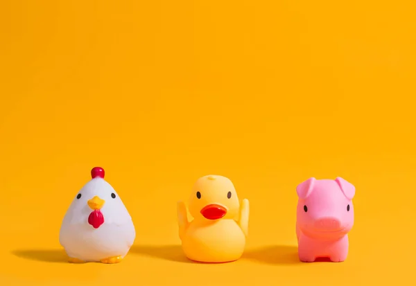 Rubber duck, pig and rooster for bathing on a yellow background. Children\'s toys. Copy space.