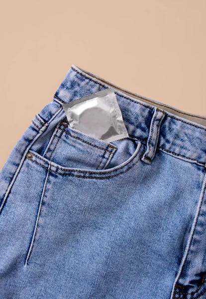 Niebieskie Dżinsy Prezerwatywą Kieszeni Beżowym Tle Przestrzeń Kopiowania — Zdjęcie stockowe