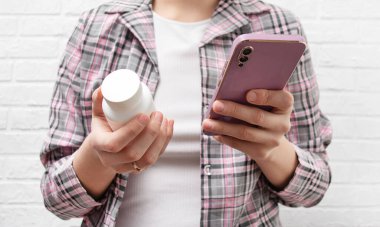 Bir kadın elinde bir kavanoz hap ve bir telefon tutuyor. Grip ilacı, ağrı kesici, vitaminler. Tıp kavramı.