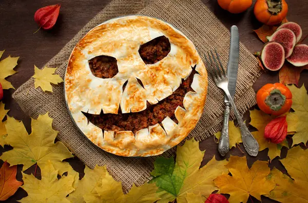 Halloween food. Homemade meat pie with a scary face for Halloween on a wooden table