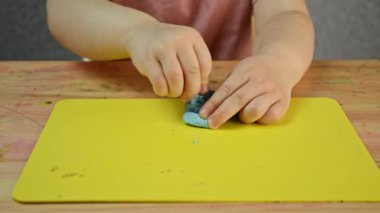 Çocuk plastikçeyi elleriyle yoğuruyor ve plastik bıçakla kesiyor. Çocukların motor becerilerinin gelişimi. Evde uzaklık öğrenimi.