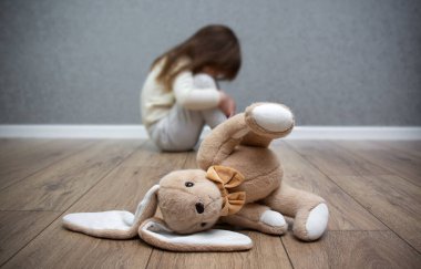 Yerde peluş bir tavşan, arkasında korkmuş bir çocuk oturuyor. Çocuk istismarı. Aile içi zorbalık..