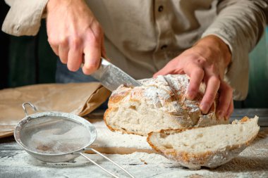 Adam tahta bir masada taze ekmek dilimliyor.