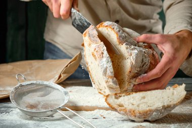 Adam tahta bir masada taze ekmek dilimliyor.